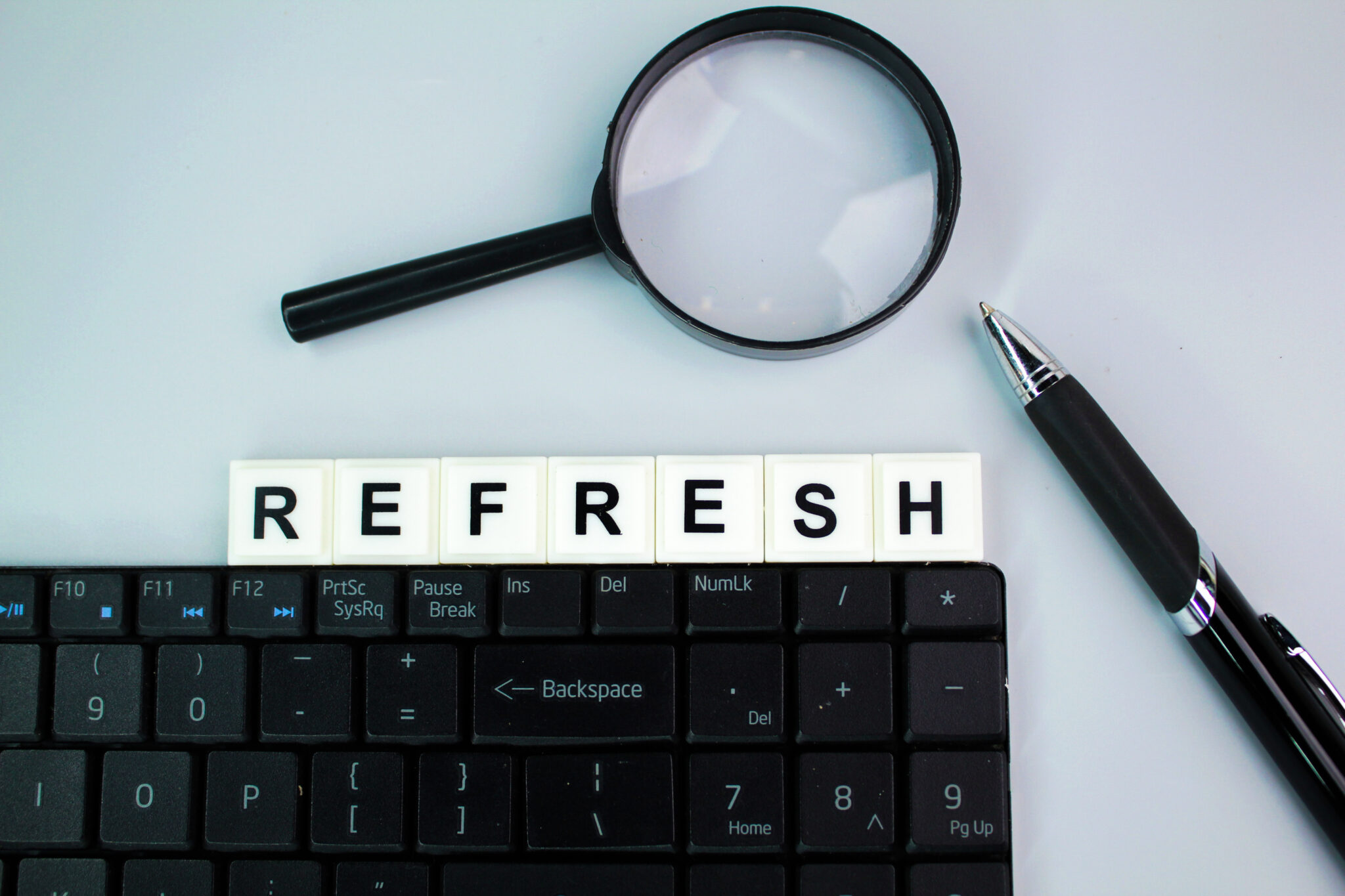 laptop keyboard, magnifying glass and pen with the word refresh.